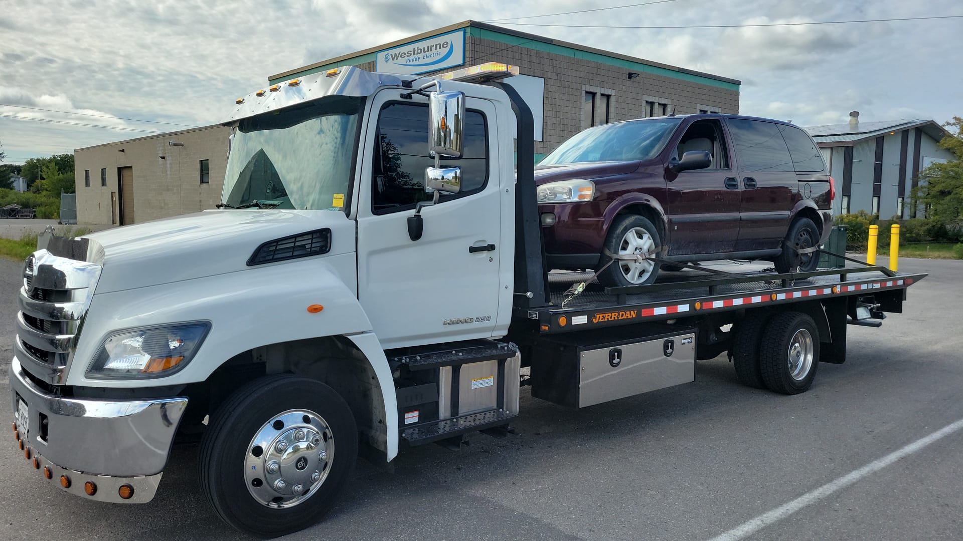 Flatbed tow truck carrying a maroon minivan at a GTA commercial location