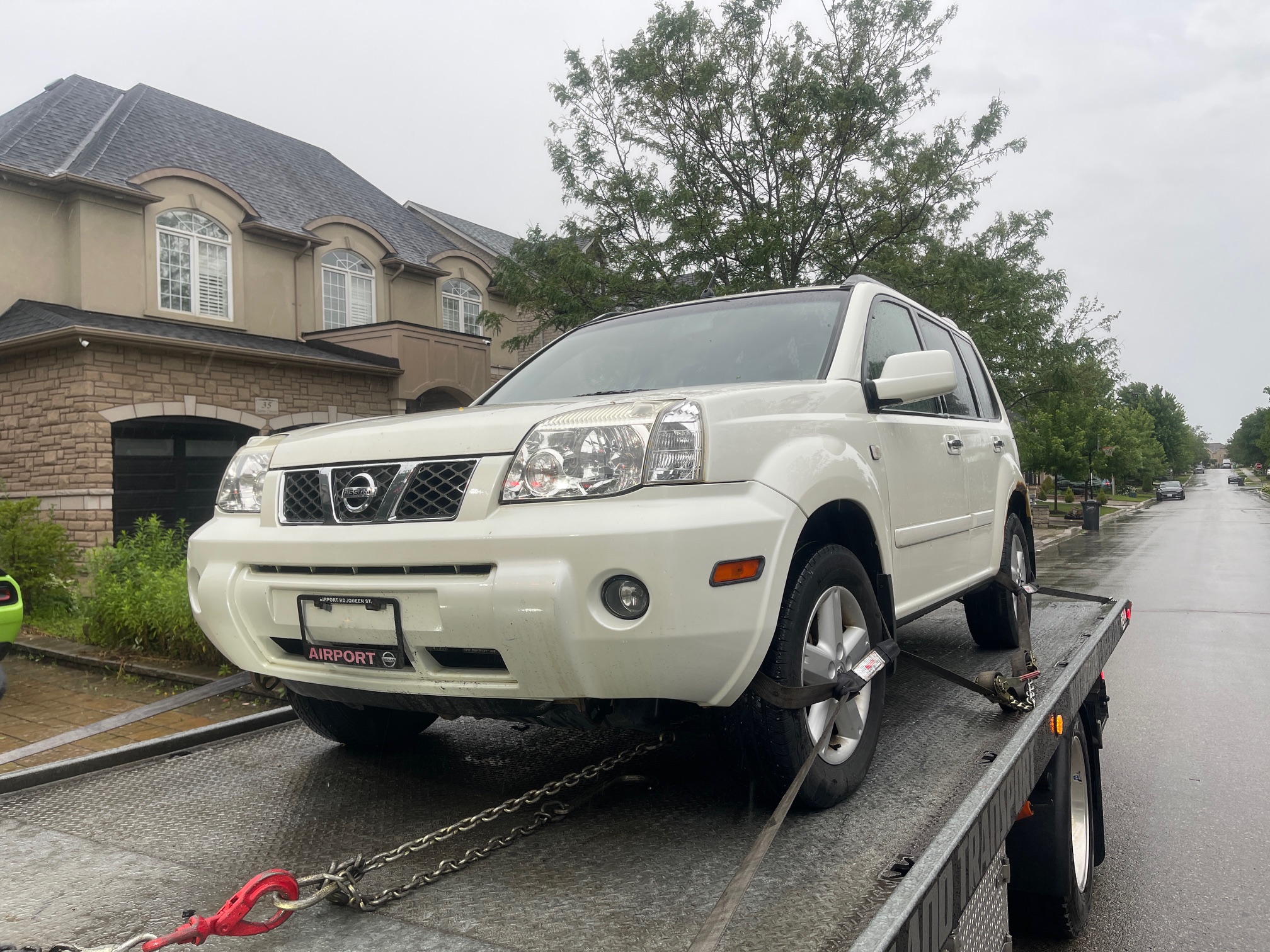 White Nissan SUV secured to a flatbed for pickup on a rainy GTA street