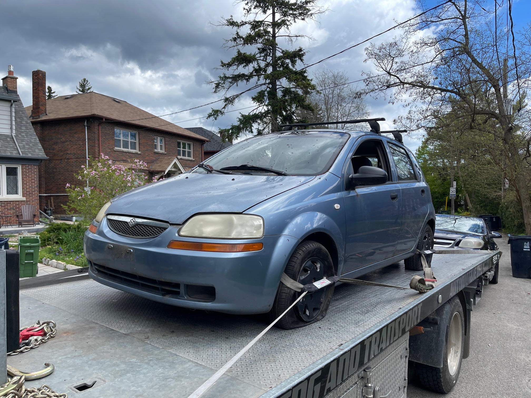 Blue hatchback secured on a flatbed in a residential Toronto neighbourhood