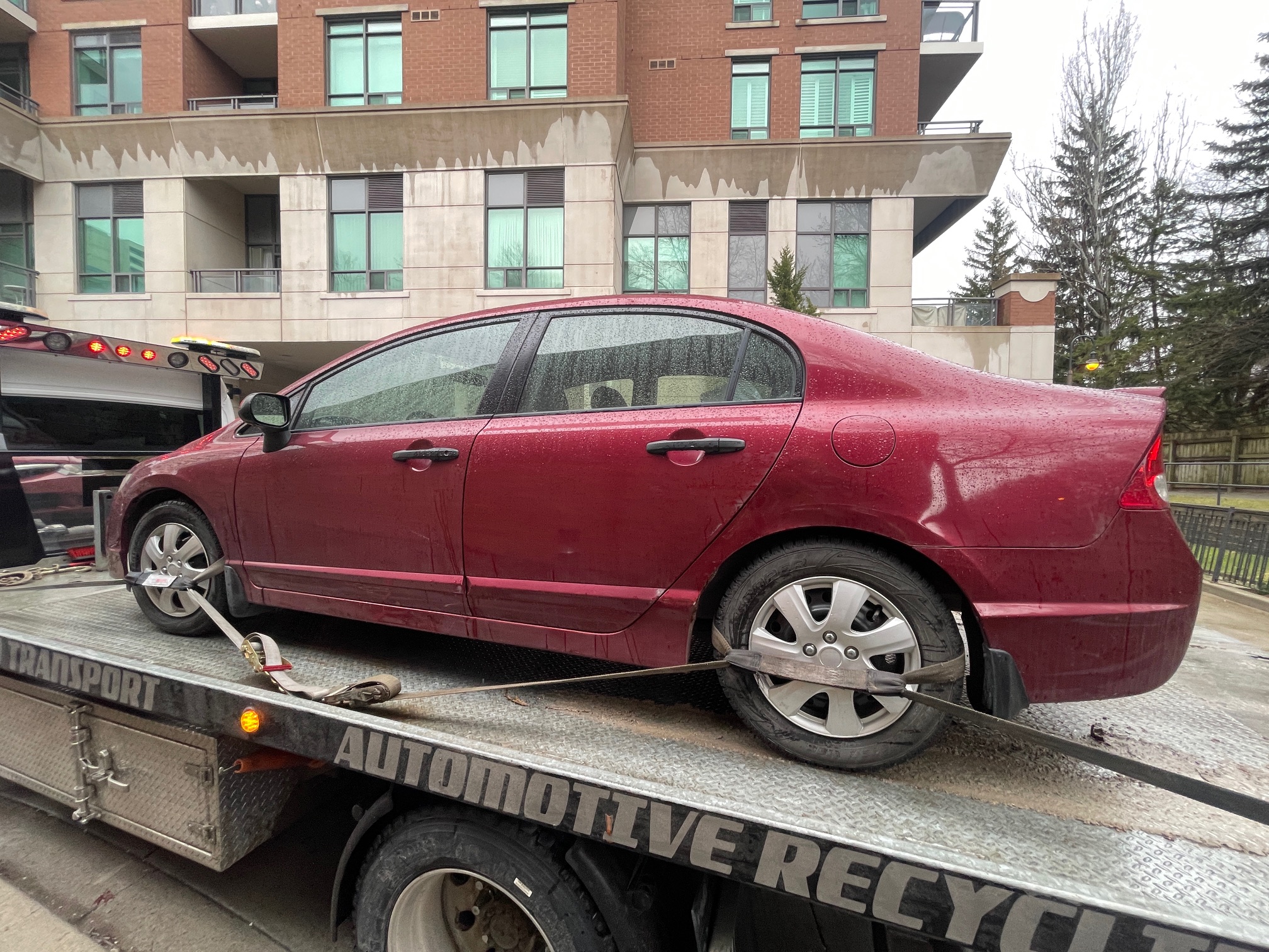 Sedan secured on a flatbed outside a condominium building on a rainy day