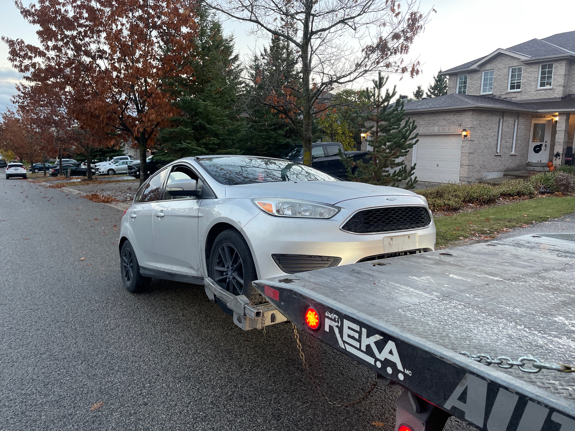 White Ford sedan beside a flatbed tow truck in a GTA residential neighbourhood