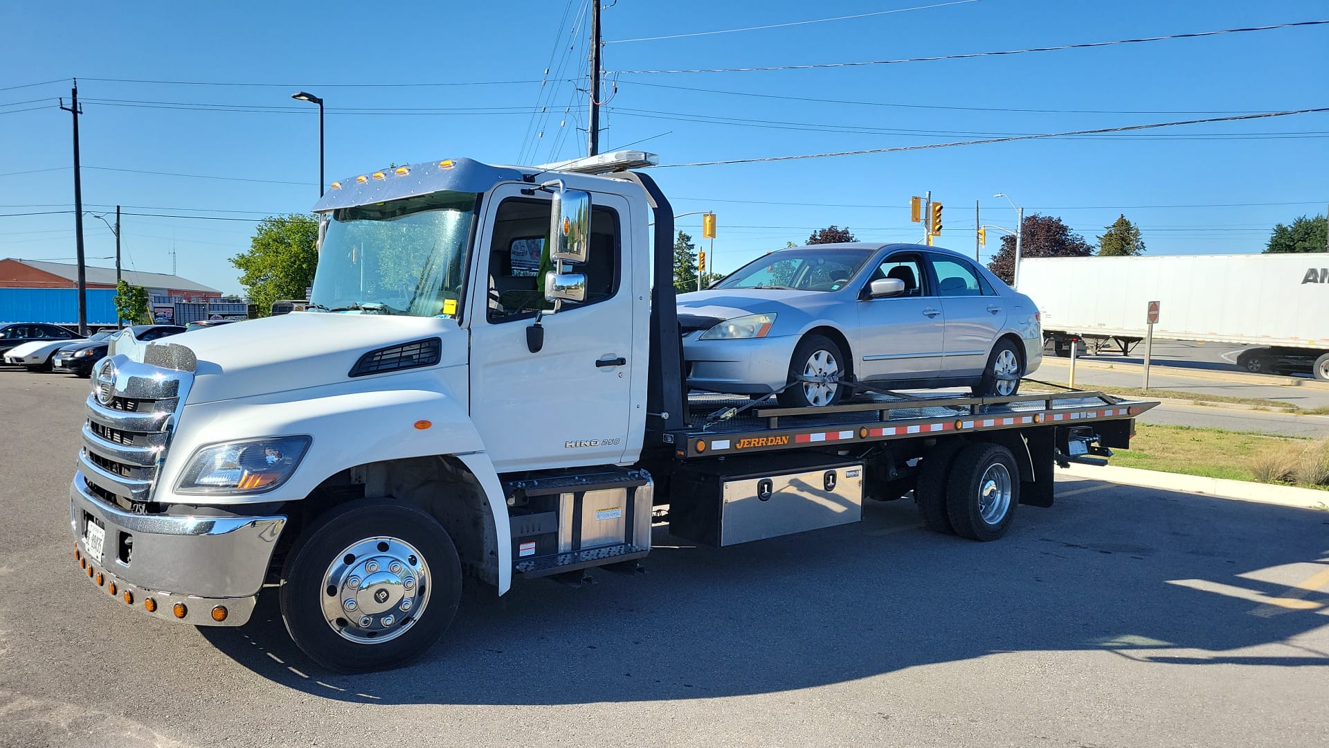 Flatbed tow truck with a silver sedan secured for pickup on a Toronto street
